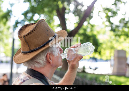 Senior thirsty tourist man drinking water from bottle in park Stock Photo