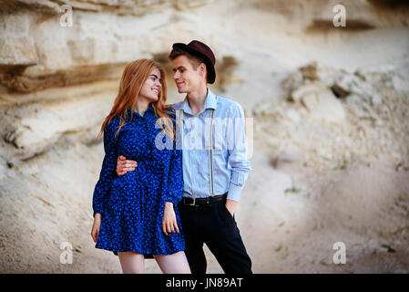 An attractive man hugs a beautiful woman in a blue dress in the middle of a sandy canyon. Lovers are happy, they are smiling to each other. Stock Photo