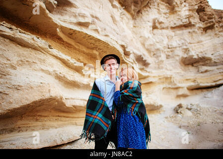 An attractive man hugs a beautiful woman. The pair wrapped in plaid in the middle of a sandy canyon. Stock Photo