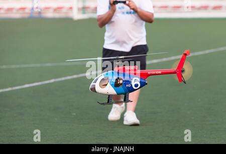 man piloting tiny radio controlled helicopter in the Football field, Spain Stock Photo