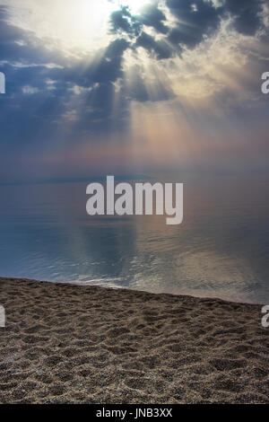 Sun beams bursting through some clouds over a calm sea Stock Photo