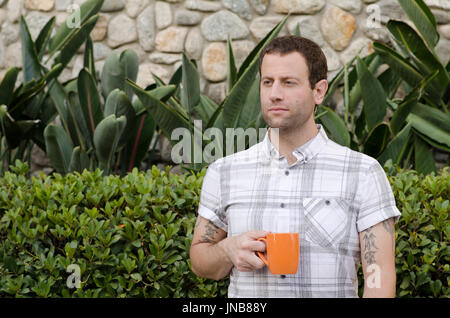 Hopeful man outdoors holding an orange coffee mug looking out to the side. Stock Photo