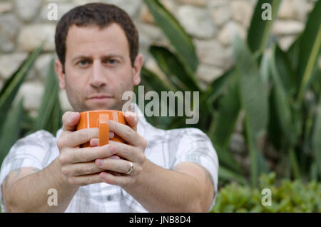 Man out of focus holding an orange coffee mug in front of him with the mug in focus. Stock Photo