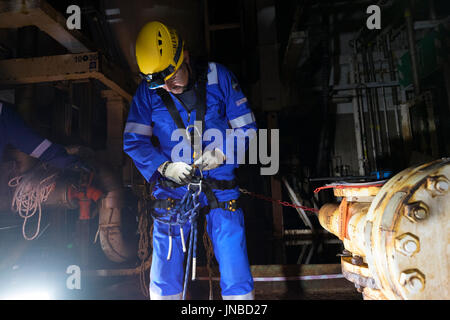 Industrial rope access technician setting up his harness, on a north sea oil and gas installation wearing Blue coveralls. credit: LEE RAMSDEN / ALAMY Stock Photo