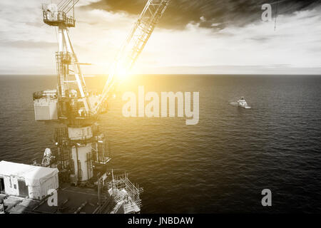 A black and white image, with sun flare, of a supply vessel and a north sea oil and gas rig crane. credit: LEE RAMSDEN / ALAMY Stock Photo