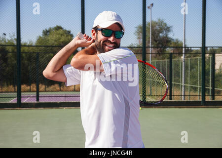 Professional tennis player with face of effort doing a tennis kick with the racket on a tennis court on a sunny day. Stock Photo