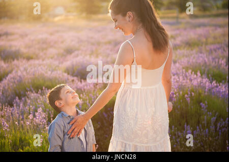 Happy smiling mother and child looking at each other with love standing among blooming lavender flower field at warm sunset Stock Photo