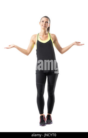 Confused young athletic sporty woman in leggings shrugging shoulders looking up. Full body length portrait isolated on white background. Stock Photo