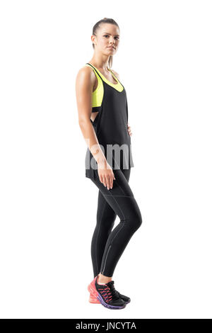 Side view of confident serious female jogger in black leggings looking at camera. Full body length portrait isolated on white background. Stock Photo