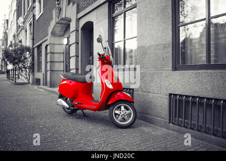 Red vintage scooter parked on sidewalk of empty city street. Selective color effect Stock Photo