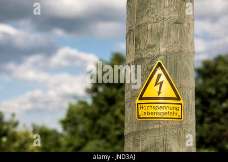 German high voltage sign mounted on wooden pole with green tree in the background Stock Photo