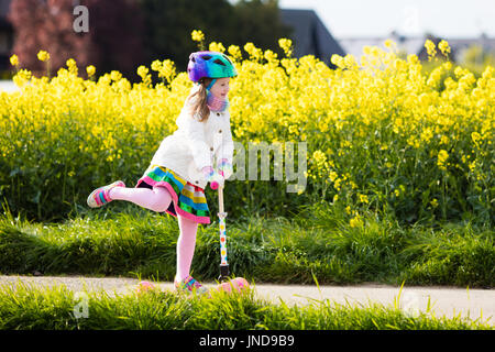 Child riding scooter on way back to school. Little girl playing outdoors learning to balance on kick board. Kids ride scooters in suburbs street. Pres Stock Photo