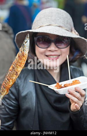 Chinese woman in sunglasses showing bought fish and seafood. Wangfujing street, Beijing, China, famous street food snack district, 5 November 2016 Stock Photo