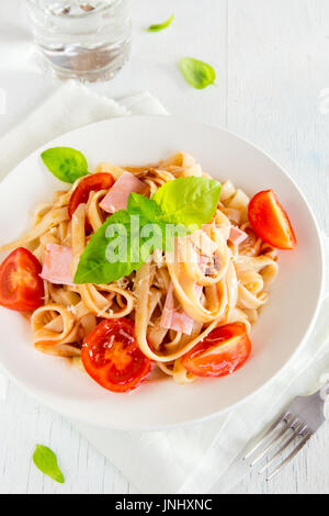 Tagliatelle pasta with ham, tomato sauce, cherry tomatoes and basil leaves on white plate - homemade delicious tagliatelle pasta Stock Photo