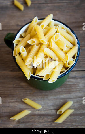 Uncooked raw italian penne pasta in metal mug - healthy ingredient for cooking pasta Stock Photo