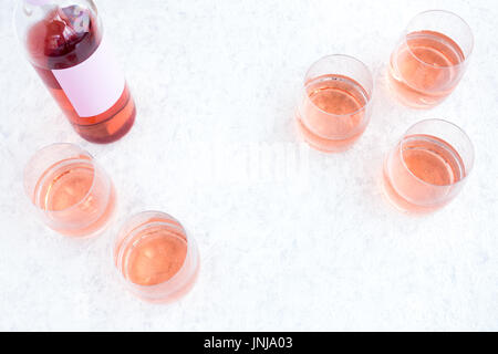 Rose Wine bottle and glasses filled with wine on white marbled background. Stock Photo