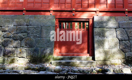 Red wooden door with stone wall at an ancient shrine in Japan. Stock Photo