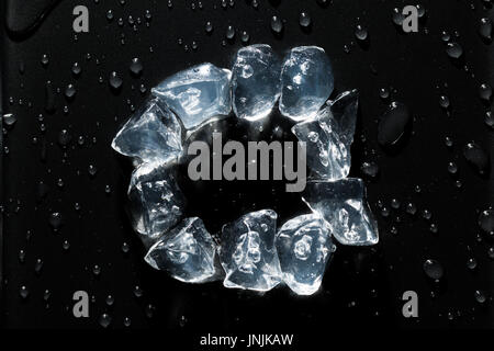 Ice cubes in a circle with water drops all around, on a black metal surface background Stock Photo