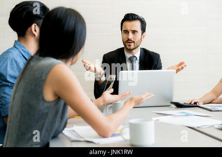 Business negotiation, male partners arguing, funny easygoing woman keeping calm in stressing situation, meditating with composed smile, dealing with e Stock Photo