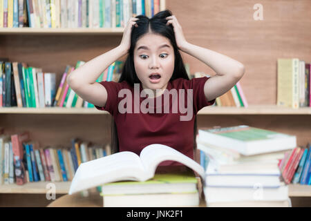 Young Asian student under mental pressure while reading book preparing examination in library at university. Asian student looking stressed. Stock Photo