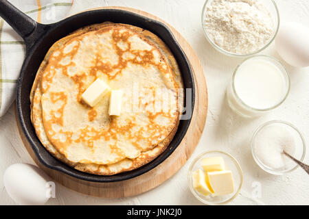 Homemade crepes with butter in cast iron pan and ingredients over rustic white background - cooking fresh homemade breakfast crepes pancakes food Stock Photo