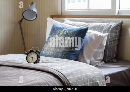black alarm clock in cozy bedroom interior with pillows and reading lamp Stock Photo