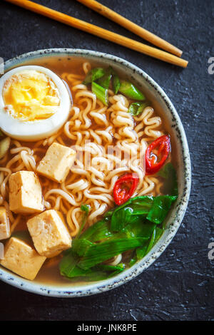 Japanese ramen soup with tofu and egg on dark stone background. Miso soup with ramen noodles and tofu in ceramic bowl, asian traditional food. Stock Photo