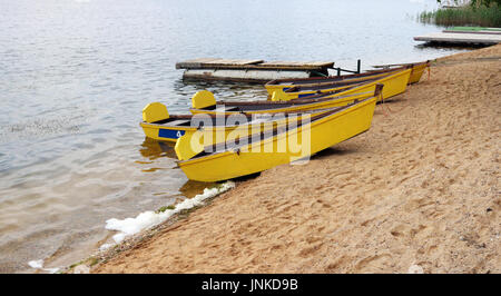 Wooden yellow aged used boats on cold fresh lake water. Sandy water coast. Cloudy day outdoor landscape Stock Photo
