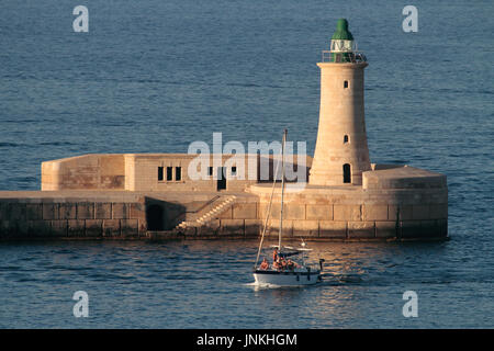 Sailing in the Mediterranean. Yacht passing by breakwater lighthouse as it enters Malta's Grand Harbour Stock Photo