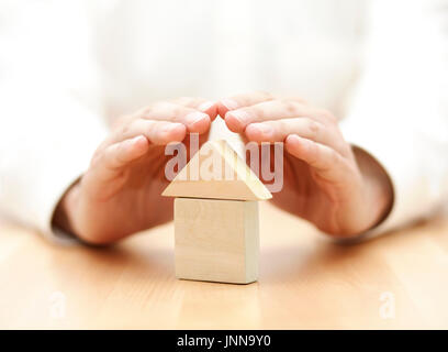 Wooden toy house protected by hands Stock Photo