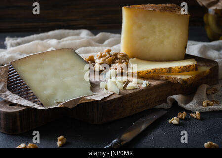 Cheese platter of chopped Spanish hard cheese manchego and sliced Italian pecorino toscano) on wooden board, with green olives in glass jar and walnut Stock Photo