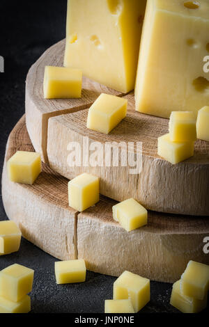 Close up of Swedish hard yellow cheese with holes chopped on wooden slices on dark rustic background Stock Photo