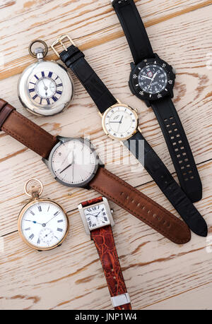 Group of four mens wristwatches, and two pocket watches on a wooden background. Stock Photo