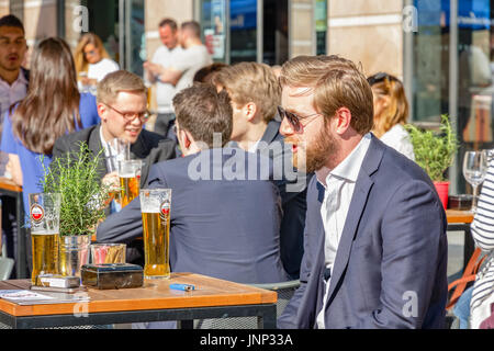 London, UK - May 10, 2017 - A young businessman at a outdoor bar in Canary Wharf packed with people drinking on a sunny day Stock Photo