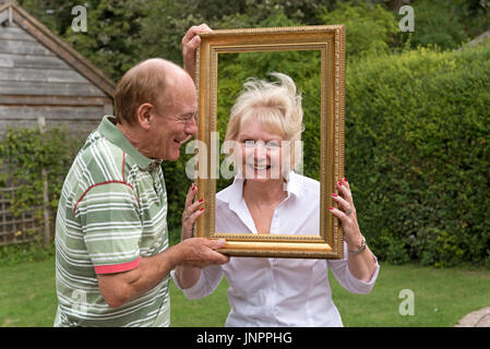 Elderly couple playing with a picture frame in a garden setting Stock Photo