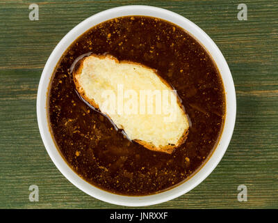 Bowl of French Onion Soup With Toasted Bread and Melted Cheese Against a Green Wooden Background Stock Photo