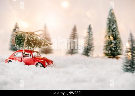 Little red car toy carrying Christmas tree in snow covered miniature forest Stock Photo