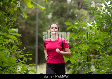 Young Woman Running In Wooded Forest Area - Training And Exercising For Trail Run Marathon Endurance - Fitness Healthy Lifestyle Concept Stock Photo