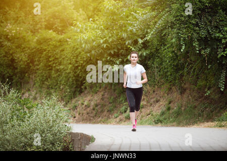 Young Woman Running In Wooded Forest Area - Training And Exercising For Trail Run Marathon Endurance - Fitness Healthy Lifestyle Concept Stock Photo