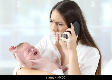 Mother calling to a doctor on phone worried about her baby crying desperately at home Stock Photo