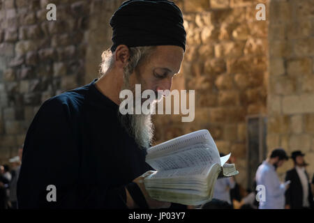 Israel, Jerusalem 31st July. Orthodox Jewish man mourning and reading from the biblical Book of Lamentation on Tisha B'Av feast at the Western Wall in Jerusalem Israel on 31 July 2017. Tisha B'Av is an annual fast day in Judaism, The fast commemorates the destruction of the First and Second Temples in Jerusalem, which occurred about 656 years apart, but on the same date. Accordingly, the day has been called the 'saddest day in Jewish history. Stock Photo