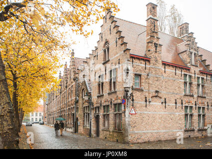 Bruges, Belgium – October 31, 2010:  A couple with an umbrella walk by old guild houses in Bruges, Belgium. Stock Photo