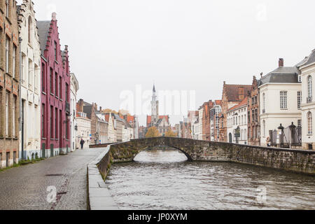 Bruges, Belgium – October 31, 2010: A few pedestrians in the rain on Spinolarei, Koningstraat bridge, the statue of Van Eyck and the Poortersloge beyond. Bruges is sometimes referred to as the Venice of the North. Stock Photo