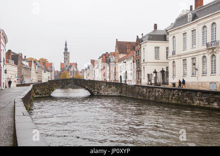 Bruges, Belgium – October 31, 2010: A few pedestrians in the rain on Spinolarei, Koningstraat bridge, the statue of Van Eyck and the Poortersloge beyond. Bruges is sometimes referred to as the Venice of the North. Stock Photo