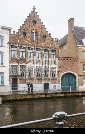 Bruges, Belgium – October 31, 2010: Couple with umbrella in front of old guild house across canal in Bruges, Belgium. Stock Photo