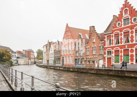 Bruges, Belgium – October 31, 2010: Pedestrians walk part guildhouses by a canal in Bruges on a rainy Autumn day. Stock Photo