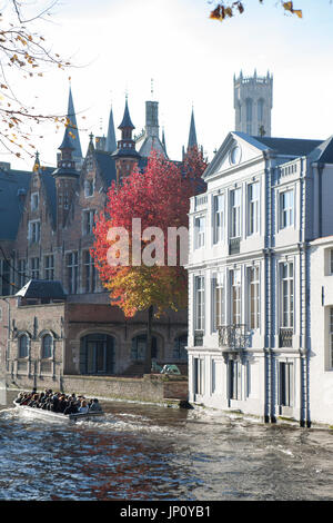 Bruges, Belgium – October 31, 2010: Boatload of tourists on the Groenerei canal in Bruges, Belgium, with medieval buildings and bright autumn foliage. Stock Photo