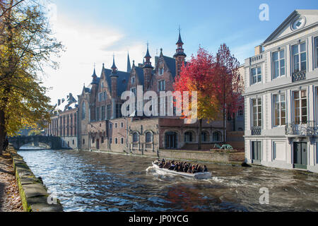 Bruges, Belgium – October 31, 2010: Boatload of tourists on the Groenerei canal in Bruges, Belgium, with medieval buildings and bright autumn foliage. Stock Photo