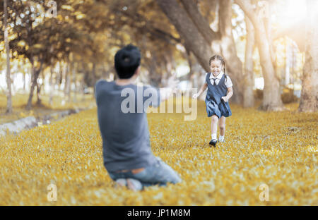 Kids student in uniform running into father's hands to hug her after back to school. love concept and vintage tone with autumn filter Stock Photo