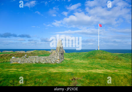 The remains of Peel Castle constructed by vikings on top of Peel hill with Isle of Man national flag on a clear blue sky Stock Photo